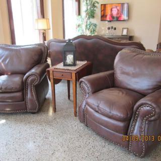 A cozy living room with leather armchairs and a sofa, accompanied by a small wooden table and a lamp.