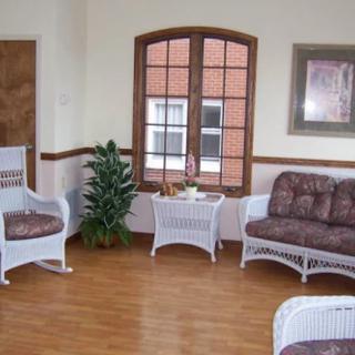 A cozy seating area with wicker furniture and a potted plant, featuring a wooden floor and large window.