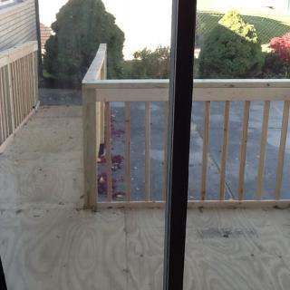 A newly constructed wooden balcony viewed through a glass door.