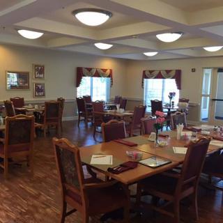 An interior view of a dining room with neatly arranged tables and chairs, featuring large windows and ceiling lights.