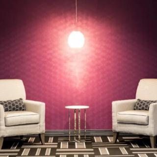 A modern living room with two white armchairs, a small round side table, and a purple accent wall illuminated by a hanging light fixture.
