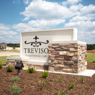 A stone and concrete sign for Treviso neighborhood set against a landscaped background.