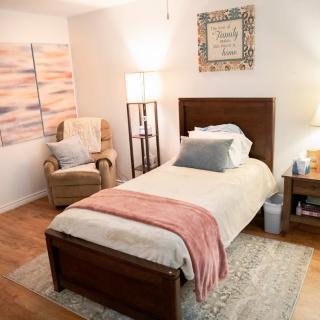 A cozy bedroom with a single bed, armchair, and soft lighting.