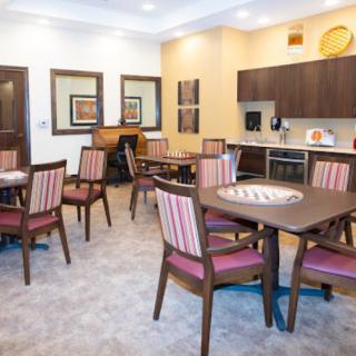 A communal dining area with multiple tables and chairs, adjacent to a kitchenette.
