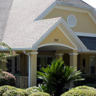 A yellow house with a porch and manicured landscaping.