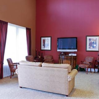 A spacious living room with red walls, featuring a comfortable sofa, television, and elegant chairs.