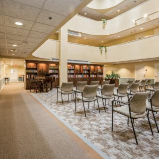 A spacious library interior with rows of chairs and bookshelves, featuring a well-lit open area.