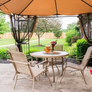 A cozy outdoor patio with a gazebo and dining set in a lush backyard setting.