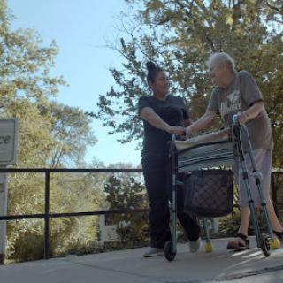 A caregiver assisting an elderly person with a walker outdoors.