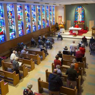 A view of a church interior showcasing stained glass windows and a gathering congregation during a worship service.