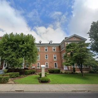 A historical brick building surrounded by trees and grass under a partly cloudy sky.