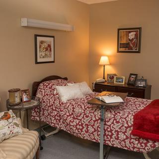 A cozy, well-decorated bedroom featuring a hospital bed with a patterned blanket and a side table with a lamp.