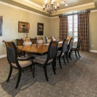 A spacious dining room featuring a long table with elegant chairs and a chandelier overhead.
