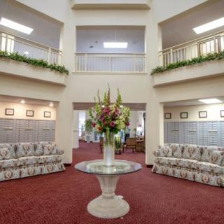 A spacious lobby featuring elegant sofas, a central floral arrangement on a glass table, and an open balcony layout.