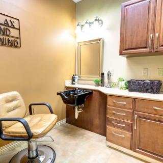 A cozy salon interior featuring a hairdressing chair, sink, mirror, and cabinetry.