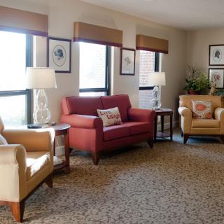 A cozy living room with sofas and armchairs, decorated with lamps and wall art.