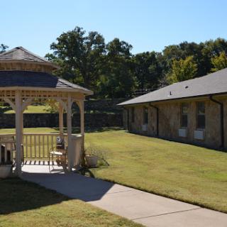 A serene outdoor space featuring a gazebo and a neighboring building under a clear blue sky.