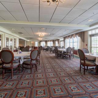 An elegant dining hall with neatly arranged tables and chairs, featuring large windows and chandeliers.