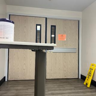A waiting area featuring double doors, a caution sign on the floor, and a container of cleaning supplies on a table.