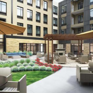 A modern apartment complex courtyard featuring outdoor seating and lush landscaping.