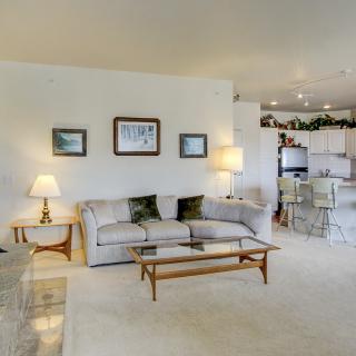 A cozy and bright living room with a sofa, coffee table, and lamps, leading into the kitchen area.