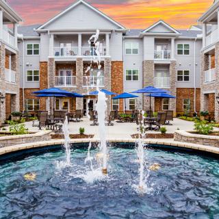 A modern apartment complex features a central fountain and outdoor seating area at sunset.