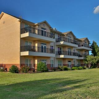A residential apartment building with balconies set against a clear blue sky, surrounded by a well-maintained lawn.