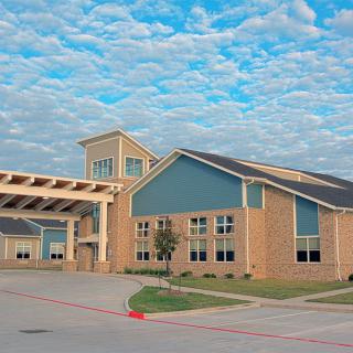 A modern school building with a covered driveway under a cloudy sky.