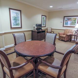 A cozy meeting room with a round table and chairs, decorated with framed paintings and warm colors.
