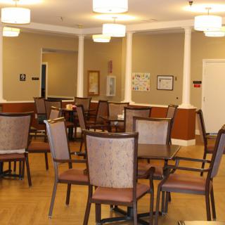 A spacious dining or meeting area with neatly arranged chairs and tables, illuminated by ceiling lights and bordered by columns.