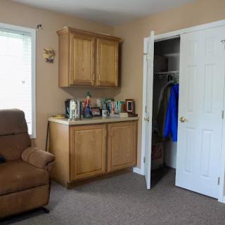 A cozy living room with an armchair, cabinet, and open closet.