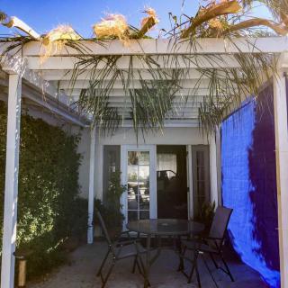 A sunny patio with a pergola, outdoor seating, and surrounding plants.