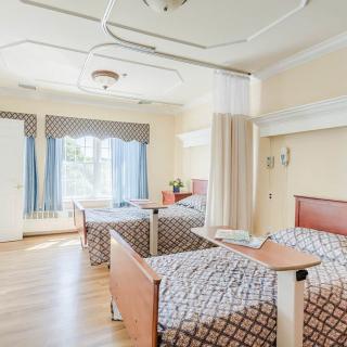 An empty hospital room with two beds and large windows letting in natural light.