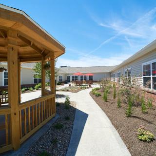 A well-maintained garden area with a wooden gazebo and pathway beside a building under a clear blue sky.