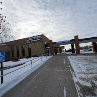 A snow-covered sidewalk leading to a modern building under a cloudy sky.