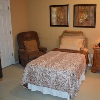 A cozy bedroom with a single bed, a comfortable chair, and wall art.