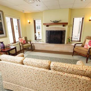 A cozy living room featuring a sofa, chairs, and a fireplace, illuminated by natural light.