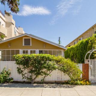 A charming suburban house with a white fence and greenery under a clear blue sky.