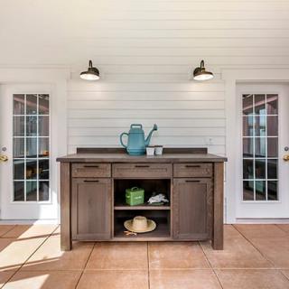 An outdoor patio setting with a wooden cabinet flanked by two glass doors, featuring stylish lighting and a decorative watering can.