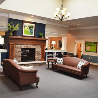 A cozy living room with a brick fireplace, elegant sofas, and a chandelier overhead.