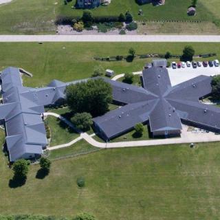 Aerial view of a uniquely shaped building with surrounding green landscape and parking area.