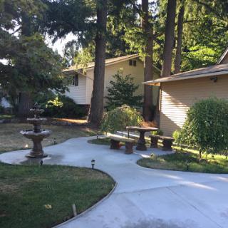 A serene garden landscape featuring a pathway, fountain, and lush greenery.