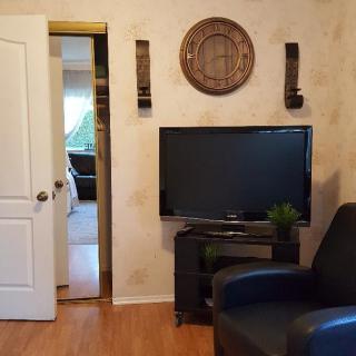 A cozy living room featuring a television, armchair, and decorative wall elements.