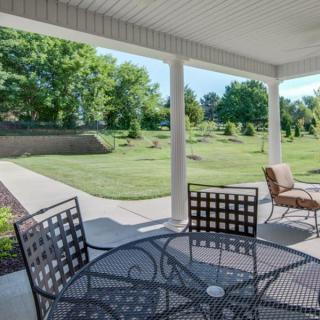 A peaceful backyard patio with outdoor seating and a view of a well-maintained lawn and trees.