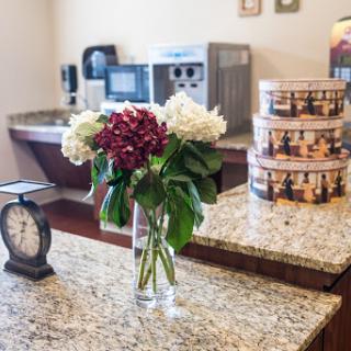 A cozy kitchen setup featuring a vibrant bouquet of flowers on a granite countertop, complemented by a vintage clock and food storage canisters.
