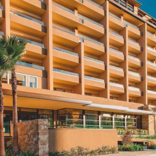 A modern hotel building with multiple balconies under a clear blue sky.