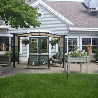 A cozy patio setup with outdoor furniture under an awning, surrounded by a well-maintained garden and lawn.