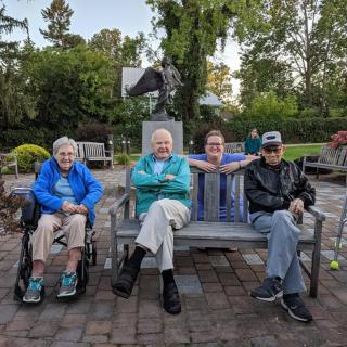 A group of four people sitting together on a bench in a garden setting.