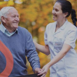 A nurse assists a senior man outdoors on an autumn day.
