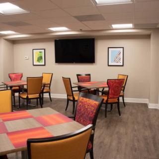 A modern dining area featuring colorful tables and chairs, with framed artwork on the walls and a television mounted above.